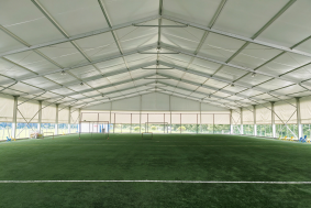Spacious interior of a clear-span sports tent by Toshimi Sports featuring artificial turf, demonstrating a pillar-free aluminum structure that maximizes playing area for commercial sports clubs.