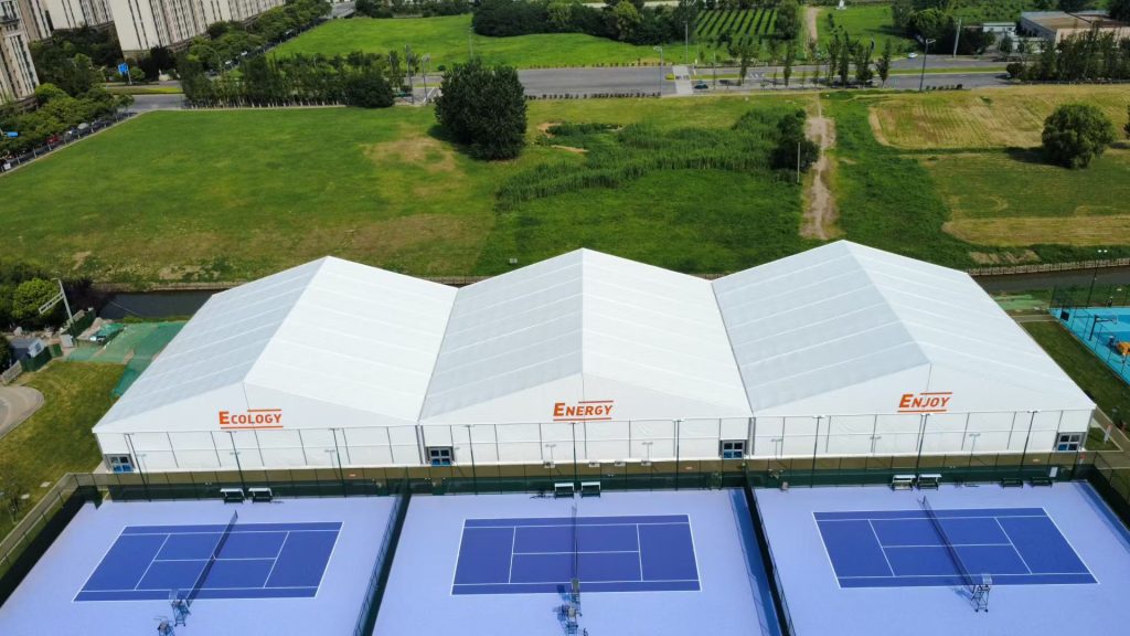 Aerial view of a commercial sports facility featuring Toshimi Sports canopies. The durable PVC fabric showcases bespoke UV-printed custom logos, covering multiple blue padel courts.