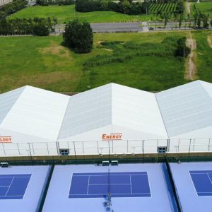 Aerial view of a commercial sports facility featuring Toshimi Sports canopies. The durable PVC fabric showcases bespoke UV-printed custom logos, covering multiple blue padel courts.