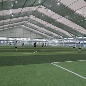 Players engaged in a game on an indoor soccer field, housed within a Toshimi Sports clear-span tent constructed purely from a heavy-duty aluminum frame and durable tarpaulin.