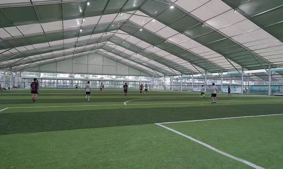 Players engaged in a game on an indoor soccer field, housed within a Toshimi Sports clear-span tent constructed purely from a heavy-duty aluminum frame and durable tarpaulin.
