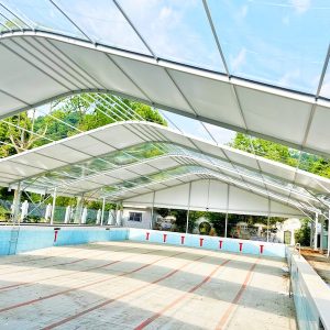 Ongoing installation of a clear-span commercial swimming pool tent by Toshimi Sports, showcasing the heavy-duty aluminum alloy frame and light-transmitting tarpaulin roof.